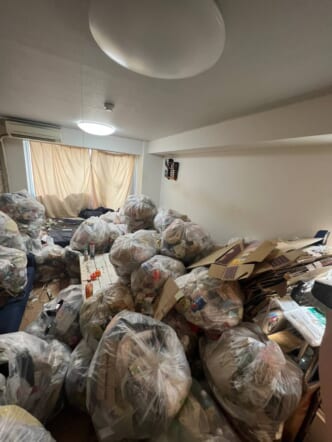 大量のゴミ袋(生活ゴミや不用品)、束ねた段ボール、古い家具などの回収前の状態