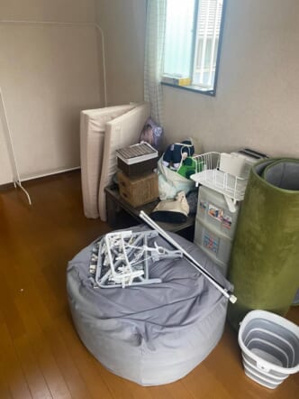 丸めたラグ、ビーズクッション、三つ折りマットレス、プラ収納ケース、洗濯ハンガー、日用品などの回収前の状態